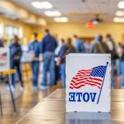 Sign with American flag and the word "Vote" sits out on a table while people mill around in the background